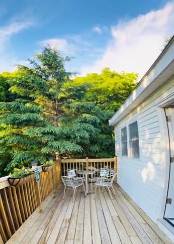A wooden deck with a small table and chairs beside tall evergreen trees