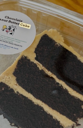 A slice of layered chocolate cake with peanut butter icing in a labeled container