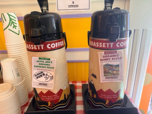 Two Carrabassett Coffee airpots on a red gingham counter
