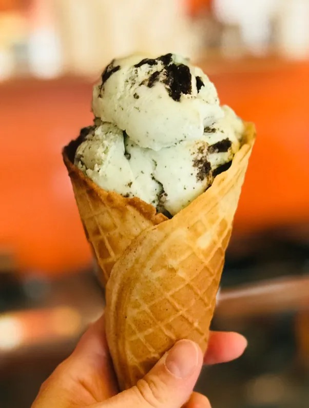 A waffle cone of cookies and cream ice cream held up in the shop