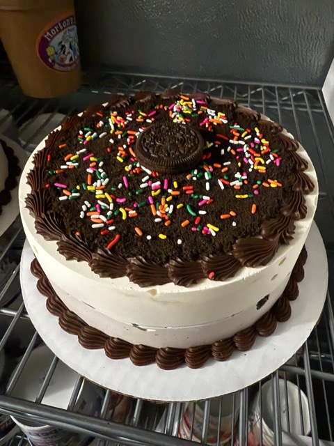 A round ice cream cake topped with chocolate crumbs, rainbow sprinkles and a sandwich cookie