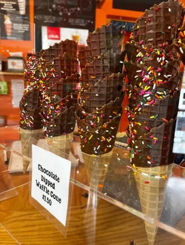 Chocolate-dipped waffle cones with rainbow sprinkles in a display