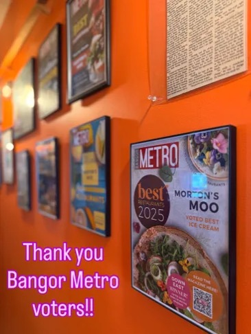 Framed magazine covers on an orange wall, including Bangor Metro’s Best Restaurants 2025 issue