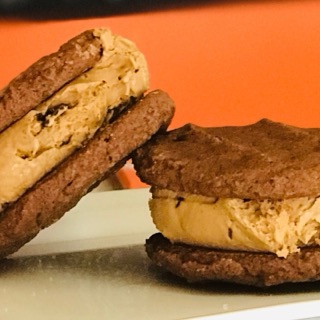 Two cookie ice cream sandwiches against an orange wall