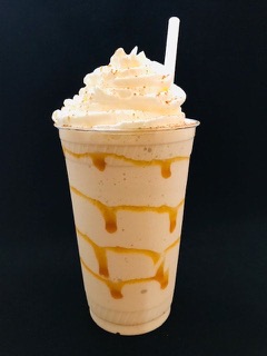 A milkshake in a tall cup with caramel swirl, whipped cream and a straw